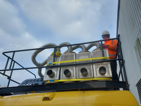Carousel 1 - site operative stood next to four powerful diesel particulate filters attached to plant machinery_