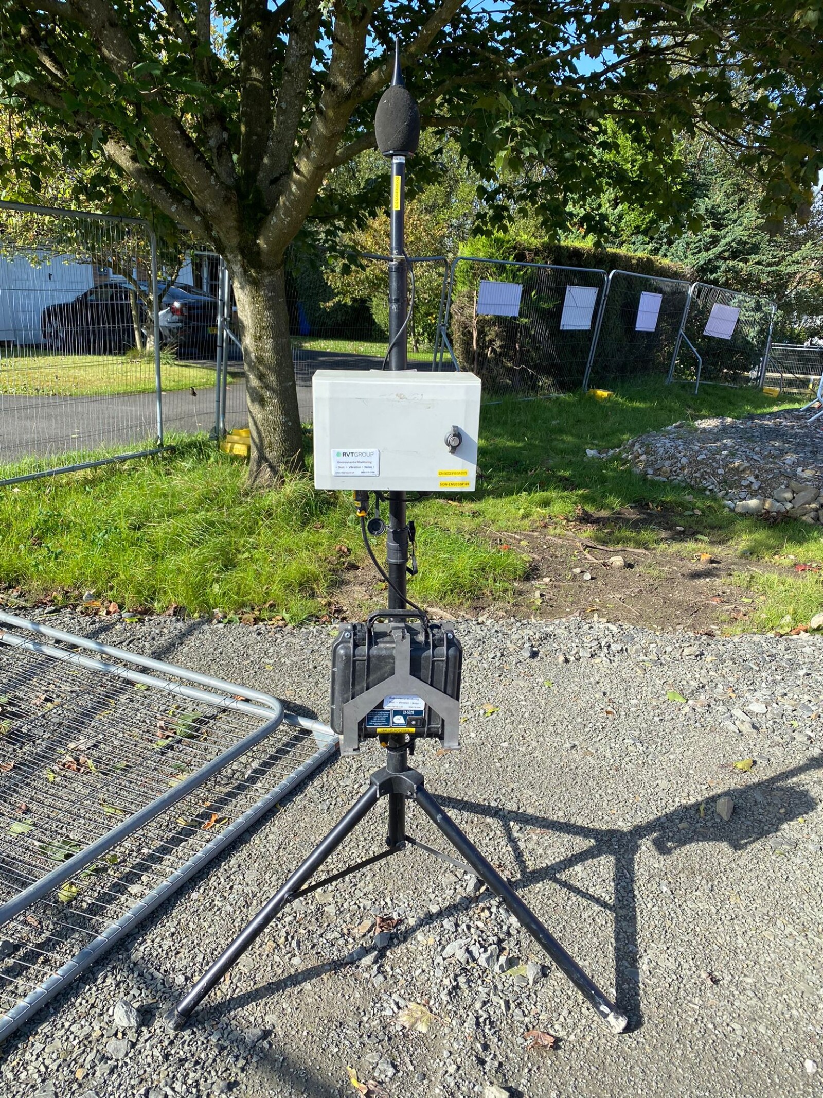 Monitex Area noise monitor on a fence line with garages and neighbouring properties in view in the background