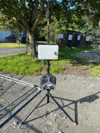 Monitex Area noise monitor on a fence line with garages and neighbouring properties in view in the background