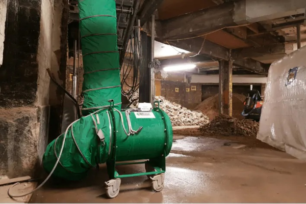 Green RVT fan on a wheeled frame with vertical ducting in a basement excavation