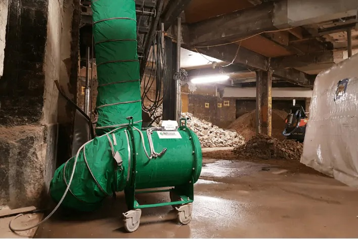 Green RVT fan on a wheeled frame with vertical ducting in a basement excavation