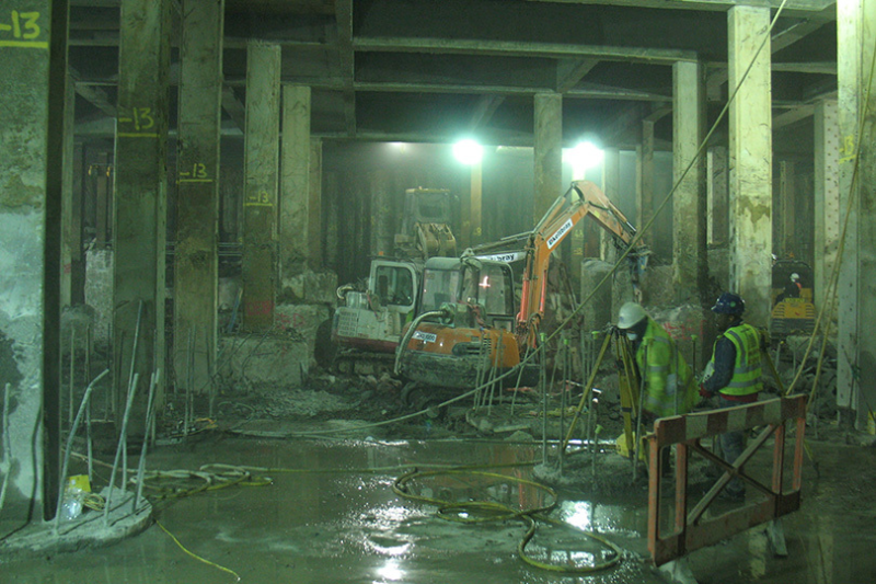 Excavator and workers breaking out concrete in a dusty basement
