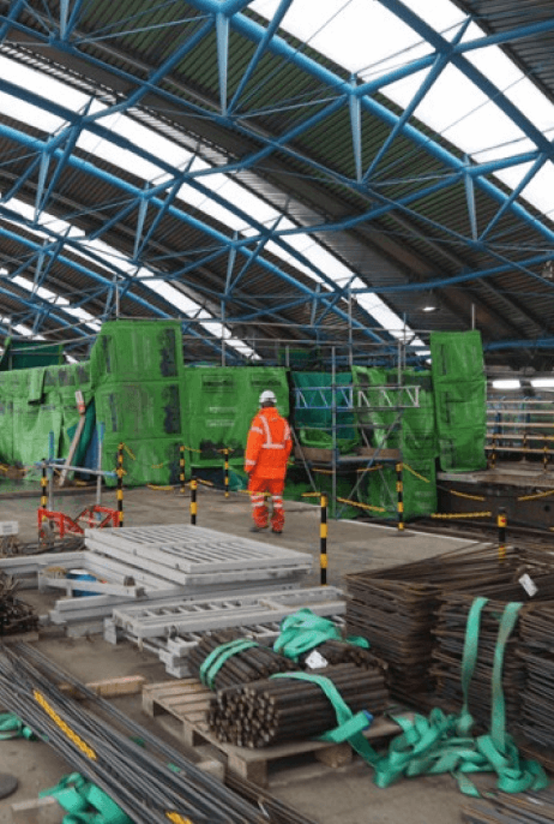 Worker beside green acoustic barriers inside a station under refurbishment