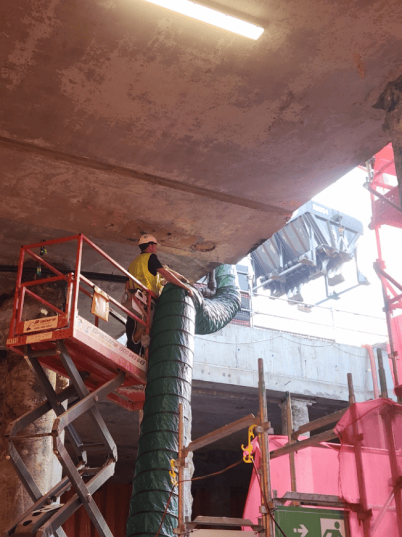 Worker on a scissor lift installing green ventilation ducting at ceiling level