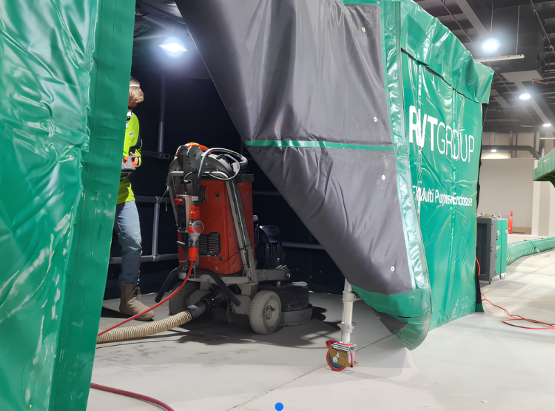Floor grinder inside an RVT dust containment enclosure with a worker alongside