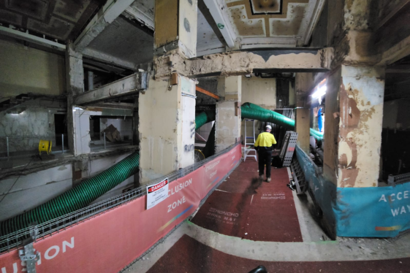 Worker walking through a heritage building strip out with green ventilation ducting overhead