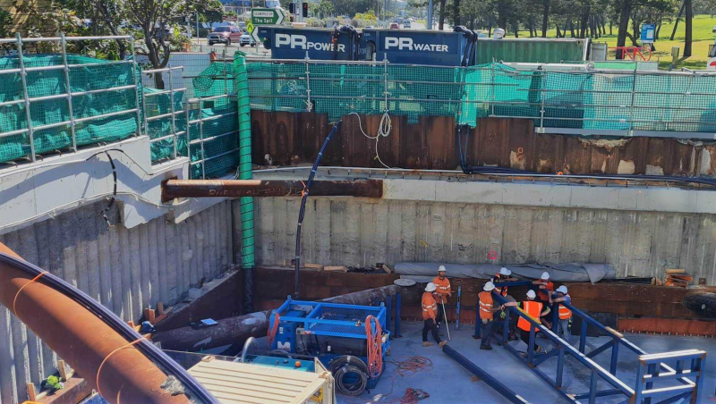 Crew working in a shored excavation with ventilation ducting and site generators