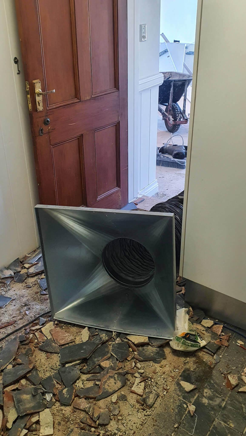 Extraction hood in a doorway with broken floor tiles on the floor