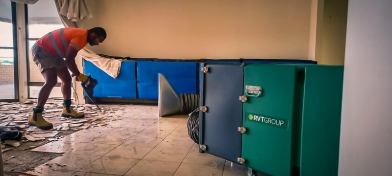 Worker lifting floor tiles beside an RVT filtration unit and dust barrier
