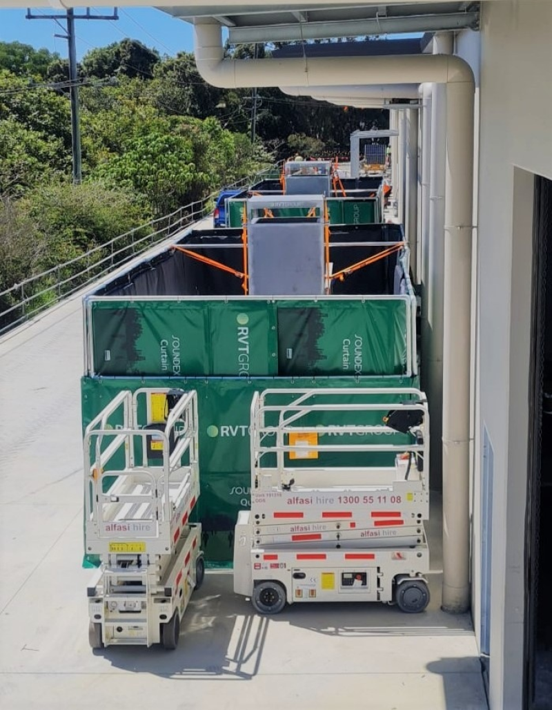 RVT acoustic curtains screening plant beside a building with scissor lifts in front