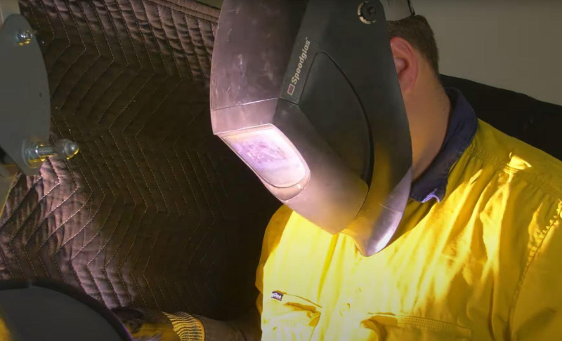 Welder in a yellow hi vis shirt wearing a welding helmet at work